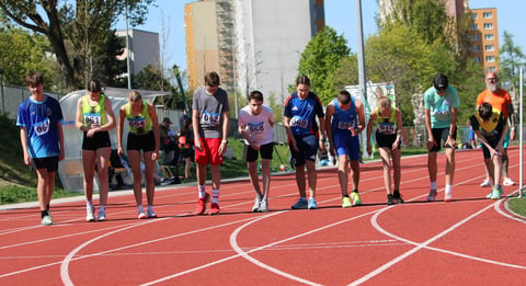 Group of young athletes standing on a red outdoor running track with city buildings in the background