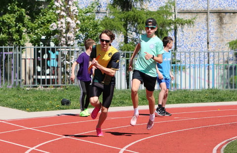Group of children running on an outdoor red track with white lane markings during a track and field event