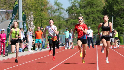 Young runners competing in a track and field race on a red athletic track with spectators watching from the sides