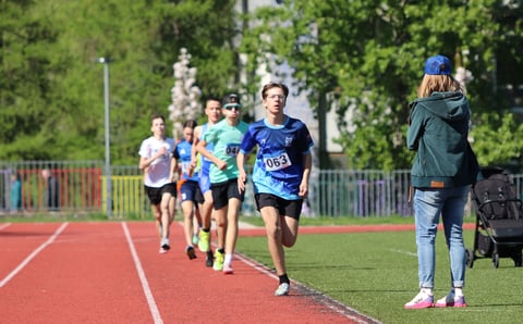 Group of young runners competing on a red track with spectator in foreground and trees in background