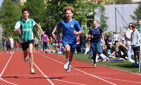 Young runners competing on a red outdoor track during a school athletic event with spectators in the background