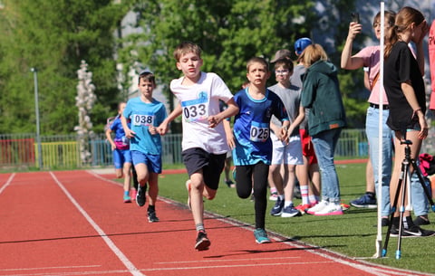 Young runners competing in a track race on a red athletic track with spectators watching from the sidelines