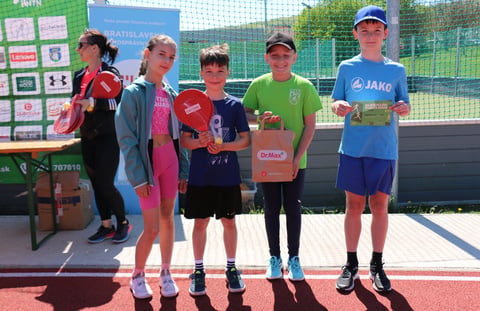 Young athletes standing on a podium holding awards at a sports event with a tennis court in the background