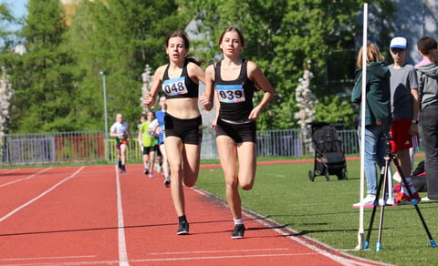 Two female runners competing on a red track during an outdoor track and field event