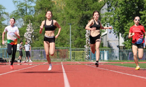 Group of runners sprinting on a red outdoor running track with green trees in the background