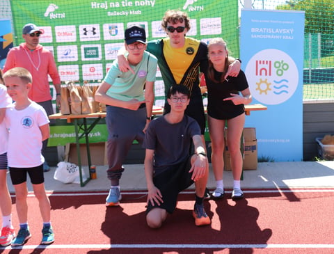 Group of children and adults on a podium at a sports event, with banners and branding visible in the background