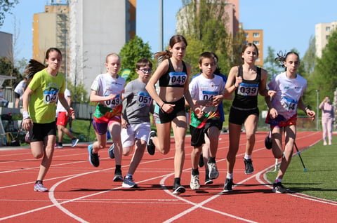 Group of young runners competing in a race on a red outdoor track with city buildings in the background