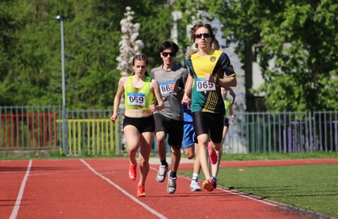 Group of young runners competing on a red track during a track and field event with race bibs