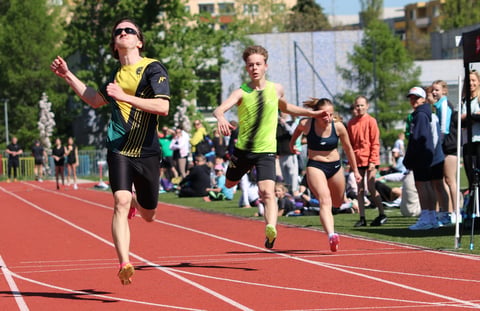 Athletes running on a red track during a race with spectators watching from the sidelines in an outdoor stadium