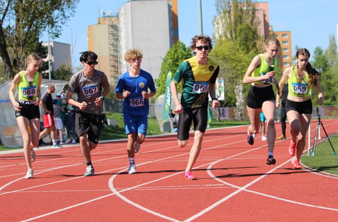 Young runners competing in a track and field race on a red outdoor track with city buildings in the background