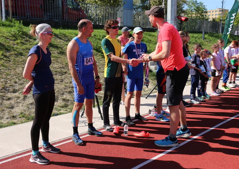 Race organizer in red shirt shaking hands with young runners on a red track during a community running event