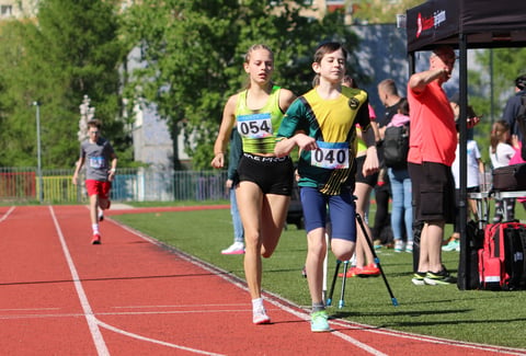 Young athletes racing on a red track during a track and field competition, with spectators watching from the sidelines