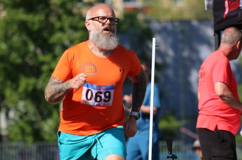 Older man with beard wearing orange race bib 069 and turquoise shorts running in a race event