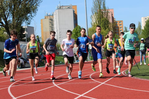 Group of young runners jogging on a red outdoor track with city buildings in the background on a sunny day